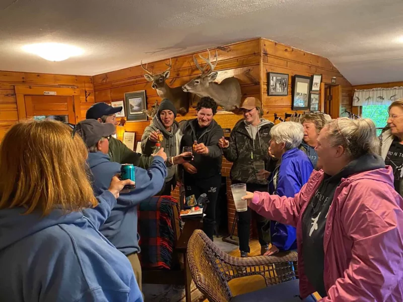 Sisterhood Travels Fly Fishing Women and fishing teachers cheering together in a cabin lobby 1920 e1686937401818 | Solo Travel For Women | Sisterhood Travels Group Tours